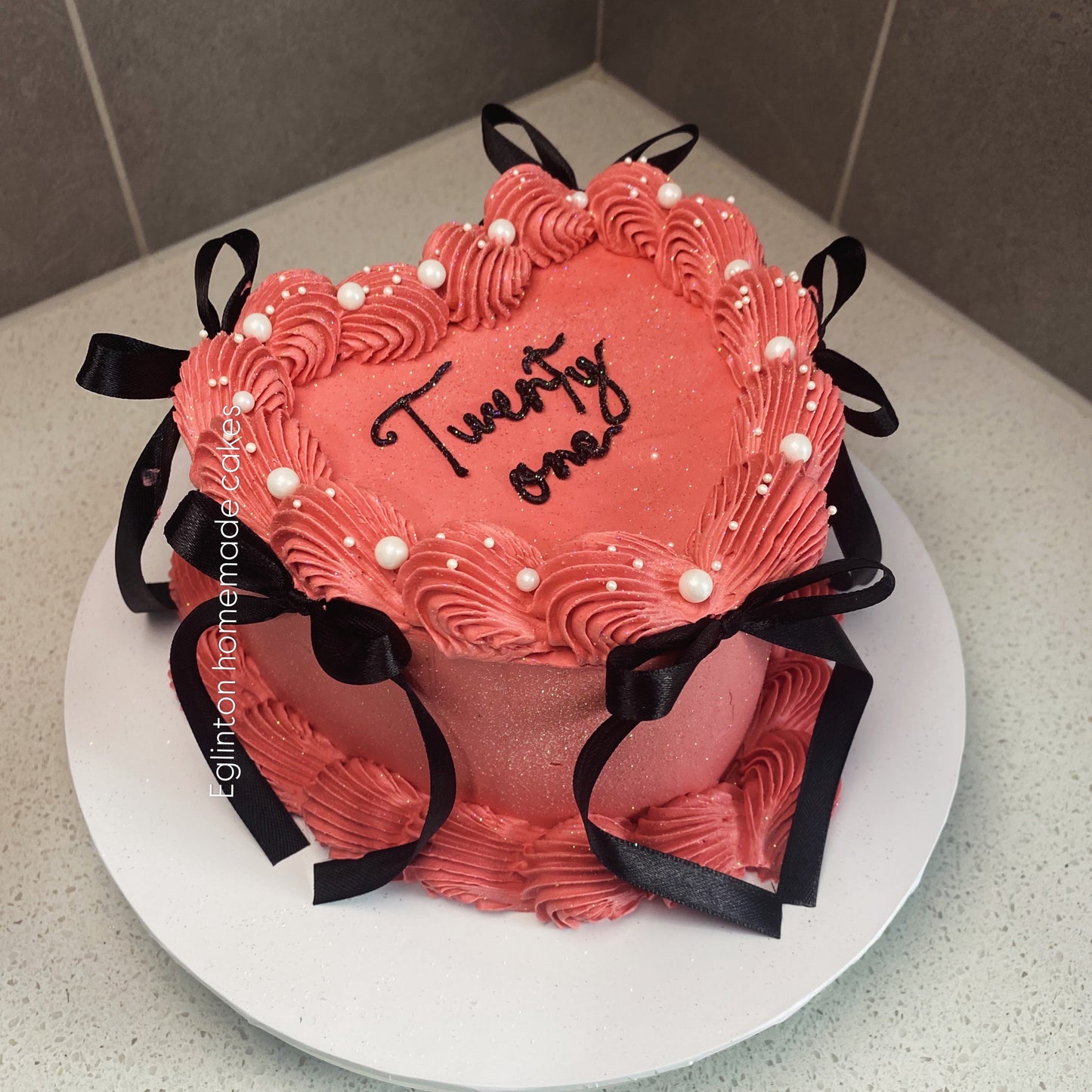 Heart-shaped pink cake with 'Twenty One' on a white plate