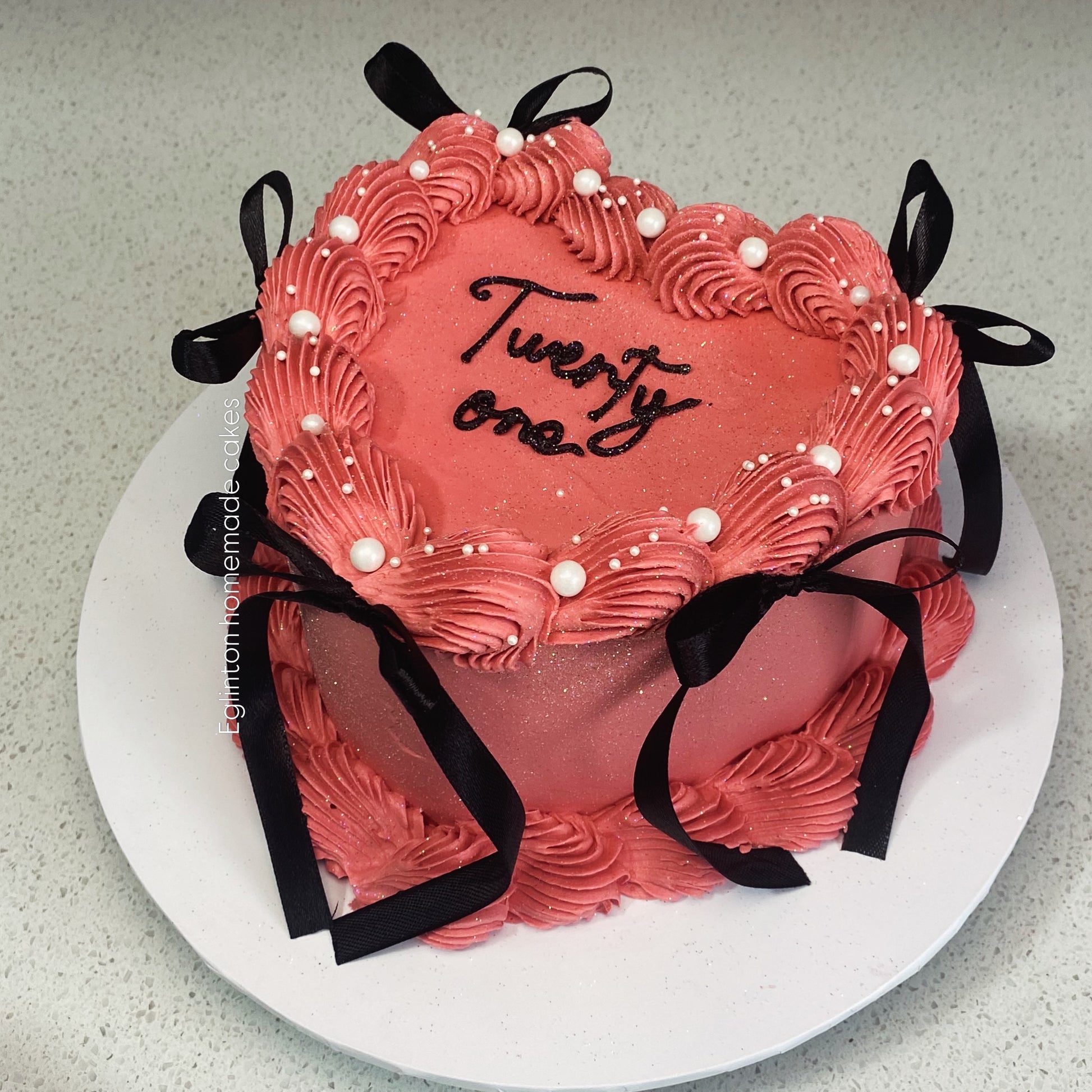 Pink cake with 'Twenty One' text and black ribbons on a white plate.